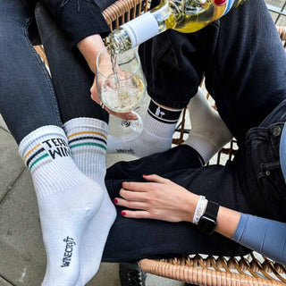 Close-up von Frauenbeinen in Winecraft-Socken beim Junggesellenabschied mit Gläsern Wein