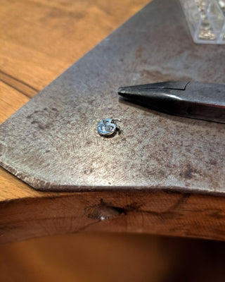 das plättchen mit der hexe liegt auf dem werktisch in der goldschmiedewerkstatt